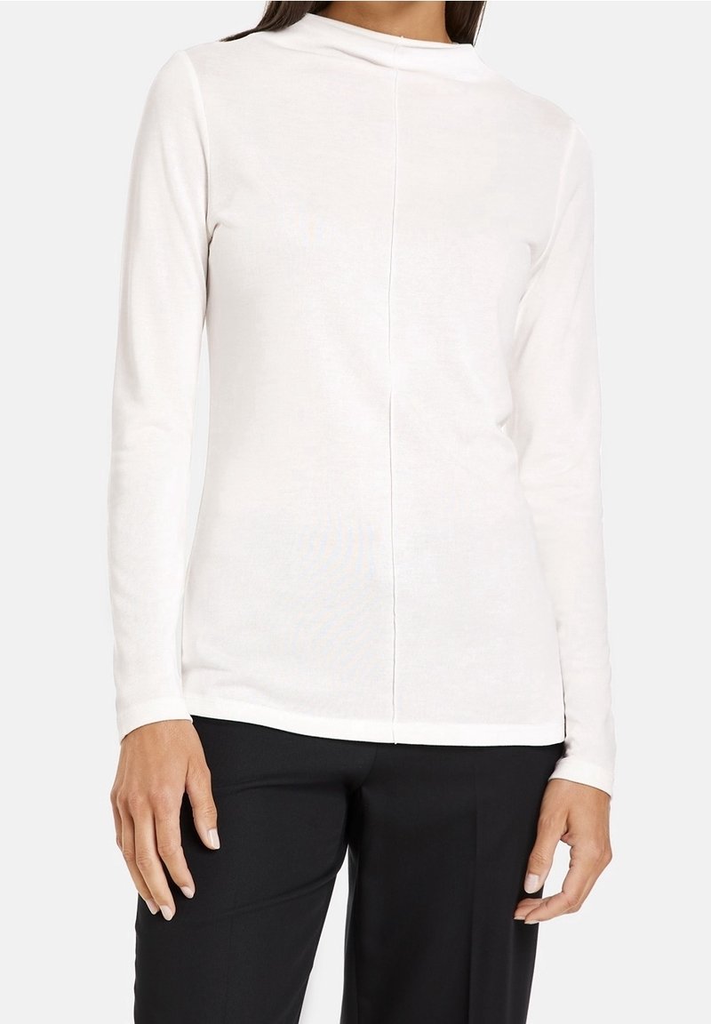 Long-sleeve, fitted top in soft white fabric with a high neck, featuring a center seam down the back and structured shoulder design.