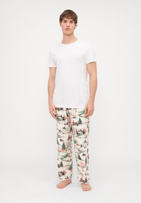 Fehér rövid ujjú póló ünnepi mintázatú pizsama nadrággal, amelyen fák, házak és havas táj látható egy világos háttéren.