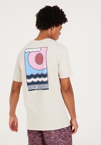 Light beige t-shirt featuring a colorful graphic design on the back with waves, a sun, and the text "WAVE CHASERS PROTEST." Short sleeves.