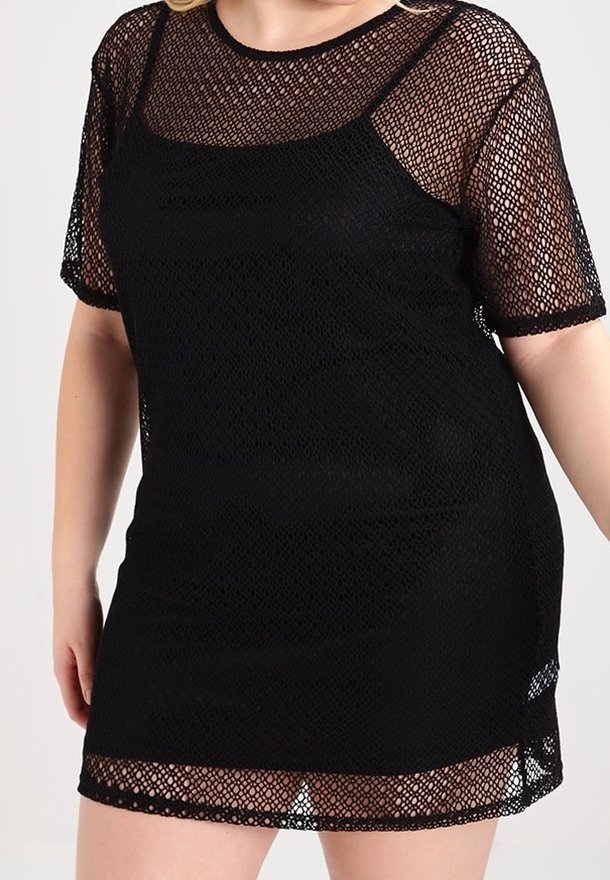 Femme portant une robe courte en maille noire avec un jupon noir uni en dessous, dotée de manches courtes et d'un col rond.
