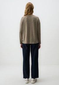 Beige strukturierter Pullover mit lockerer Passform, Rundhalsausschnitt und überschnittenen Schultern, kombiniert mit dunkelblauen weit geschnittenen Jeans und weißen Sneakers.