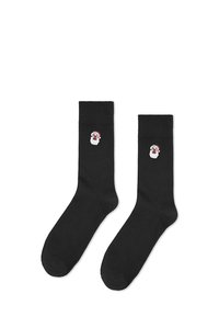 Czarne skarpetki z haftowanym wzorem twarzy Świętego Mikołaja w czerwonym kapeluszu. Wykonane z miękkiego materiału, o gładkiej fakturze i standardowym kształcie skarpetki.