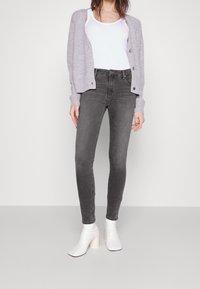 Jeans ajustados grises combinados con un cárdigan gris claro y botines de tacón blancos, mostrando un tejido texturizado y una silueta ajustada.