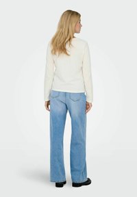 Langærmet cremetop kombineret med lyseblå, højttalende bredbenede jeans. Har baglommer og mørkt fodtøj. Enkel design, afslappet pasform.