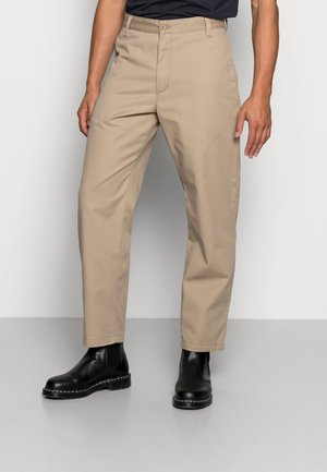 Chinos de algodão bege com pernas retas, bolsos frontais e fecho com botão, emparelhados com botas de tornozelo pretas com sola texturizada.