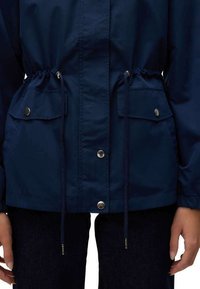 Veste légère bleu marine avec cordons à la taille, fermetures à boutons-pression et deux poches avant avec rabats.