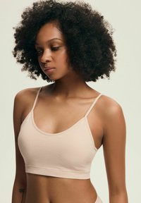 Jasno beżowy biustonosz typu braletka z cienkimi ramiączkami, bezszwowym wykończeniem oraz miękką, gładką fakturą. Posiada wyprofilowany dekold i dopasowany krój.