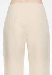 Pantalones beige de pierna ancha hechos de algodón. Tejido suave y ligero con un diseño limpio y simple y corte recto. Sin bolsillos visibles ni adornos.