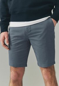 Pantalones cortos de algodón gris para hombre con un diseño de frente plano, bolsillos laterales visibles y corte recto, que llegan hasta la mitad del muslo.