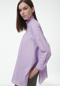 Lavender knoop-up shirt met een hoge kraag, met horizontale plooien over de voorkant en een gebogen zoom. Lange mouwen met knoopmanchetten.