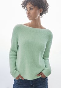 Suéter verde menta de corte relajado, con escote off-shoulder, mangas largas y suave tejido de punto texturizado. Presenta bolsillos frontales.