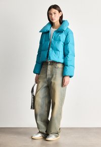 Skraćena puffer jakna u svijetloj tirkiznoj boji, sa velikim kragnom i kopčanjem na dugmad, u kombinaciji sa širokim izbleđenim farmerkama i srebrnim patikama.