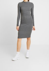 Abito midi grigio a coste con maniche lunghe e scollo alto. Presenta una silhouette aderente e una texture liscia. Indossato con sneakers bianche.