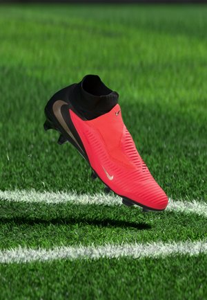 Rood-zwarte Nike voetbalschoen zweeft boven groen gras nabij een witte veldlijn.