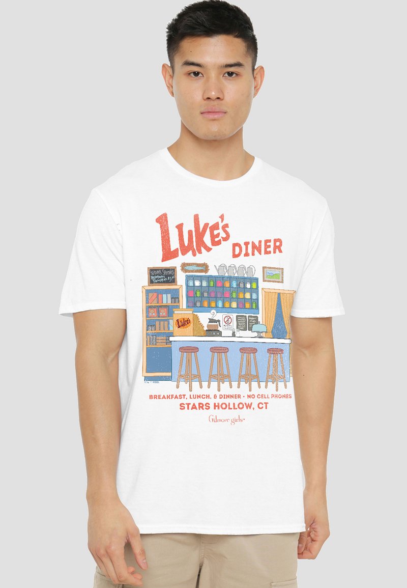 Young man wearing a white T-shirt with a colorful diner counter illustration and the text "Luke's Diner, Stars Hollow, CT."