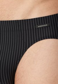 Schwarze Schwimmbriefs mit schmalen vertikalen Streifen, aus dehnbarem Material. Verfügt über ein Markenetikett, Taillennaht und eine glatte Textur.
