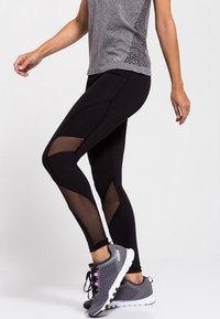 Czarne legginsy sportowe z siateczkowymi panelami, z dopasowanym krojem i kontrastującymi szwami. W zestawie z szarym t-shirtem z krótkim rękawem i szarymi sneakersami.