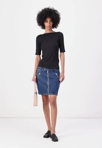 Svart tettsittende topp med korte ermer, sammen med en blå denim blyantskjørt med forhånds glidelås og sidelommer. Bærer en beige håndveske.