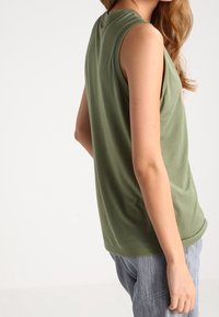 Olivgrön ärmlös topp med rund halsringning och mjukt bomullsmaterial. Designad för en avslappnad passform, med synliga axelsömmar.