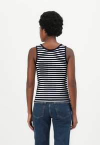 Camisola sem mangas às riscas azul-marinho e branca, com decote redondo e textura canelada, combinada com jeans azuis. A vista traseira mostra um design ajustado.