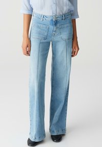 Light blue denim flared trousers with a high waist, two back pockets, and visible stitching detail. Smooth texture, wide legs, and clean finish.