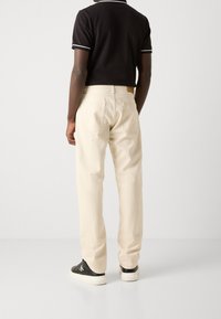 Béžové bavlněné kalhoty se střihovým designem rovného nohavice a zadními kapsami, doplněné černým polokošilem s bílými pruhovanými detaily.