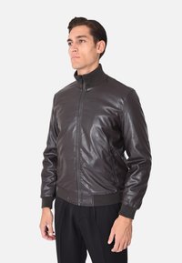 Giacca bomber in pelle marrone con chiusura a zip, colletto e polsini a coste, dotata di tasche laterali e dalla texture liscia. Adatta per un abbigliamento casual.