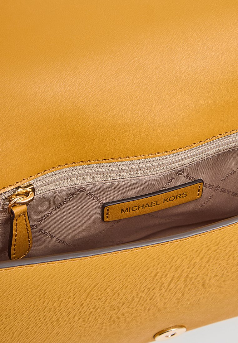Gelber synthetischer Handtaschen-Innenraum mit einem Reißverschlussfach; enthält ein goldfarbenes Michael Kors-Label auf einem hellbraunen Innenfutter. Glatte Textur.