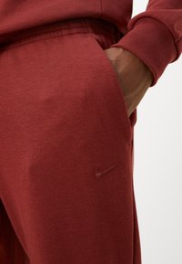 Bordowe dresy wykonane z mieszanki bawełnianej. Posiadają elastyczny pas, boczne kieszenie oraz małe haftowane logo Nike.