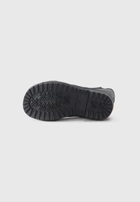 Semelle de chaussure noire avec un motif de semelle profond et robuste pour une meilleure traction. Présente des rainures prononcées et une surface texturée pour la durabilité.