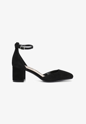 Schwarze Wildleder-Blockabsatzschuhe mit einem Knöchelriemen, spitzem Schuhkopf und ausgeschnittenen Seiten, ausgestattet mit einem glatten Innenraum und einer strukturierten Außenseite.
