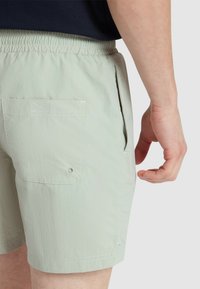 Pantaloni alta vita di colore verde chiaro realizzati in tessuto testurizzato, dotati di una vita elasticizzata, tasche laterali e una tasca posteriore con chiusura a bottone.