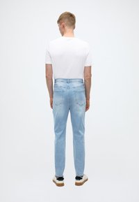 Ljusblåa jeans i denim med rak skärning, midjeficka i midjan, bakfickor och en blekt textur. Matchas med en vit t-shirt.