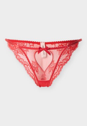 String en dentelle rouge avec motif floral, devant en résille transparente, fines bretelles sur les côtés et petite décoration en forme de nœud au centre de la ceinture.