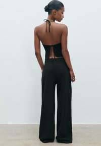 Crni halter top s vezanjem na leđima. Uparen s širokim crnim hlačama. Glatka tkanina s opuštenim krojem i minimalističkim dizajnom.