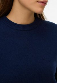 Tumši zils adīts džemperis ar ribveida apaļu apkakli, kas izceļas ar mīkstu tekstūru un gludu apdari.