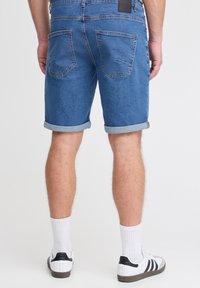 Denimshortsit keskiharmaansinisinä, joissa on kääritty reunus, kaksi takataskua ja nahkainen merkki vyötäröllä. Yhdistetty valkoisiin sukkiin ja lenkkareihin.