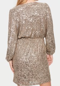 Kort klänning i ett skimrande, paljettmaterial med en figursydd midja, långa ärmar och en rund halsringning i gyllene nyans.