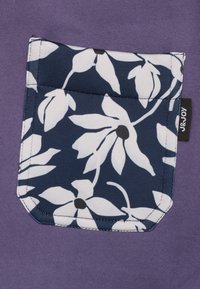 Paarse stof met een marineblauwe zak voorzien van een wit bloemmotief. Zak heeft afgeronde hoeken en zichtbare stitching. Merktag is aan de zijkant genaaid.
