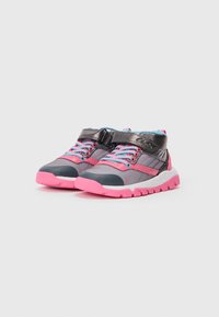 Par de zapatillas deportivas infantiles en gris con suelas rosas, cordones azules y correas de Velcro negras sobre un fondo blanco liso.