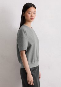 Gray short-sleeve sweatshirt with a round neckline, soft texture, and a relaxed fit, paired with a black leather skirt.