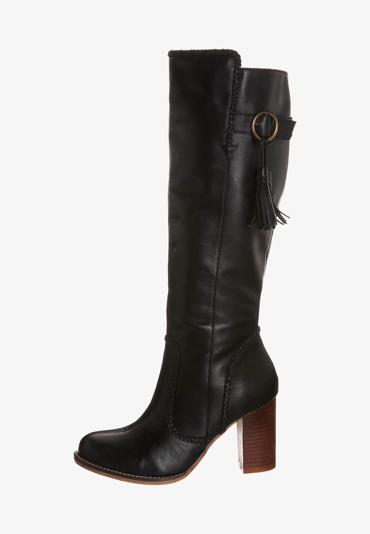 Botte noire en cuir montant jusqu'au genou avec un talon bloc, présentant un détail tressé, un pompon décoratif et un accent de quincaillerie circulaire.