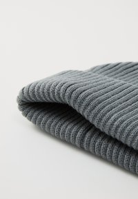Gray knitted beanie with a ribbed texture, featuring a folded cuff detail. The material appears soft and flexible.