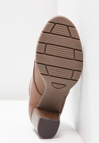 Semelle de chaussure à talon marron avec des motifs rectangulaires et le numéro de taille 37 embossé au centre près de la voûte plantaire.