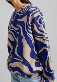 Tröja i blått och beige med vågigt mönster. Har rund halsringning och avslappnad passform. Tillverkad i ett mjukt material, som visar upp unika designelement.