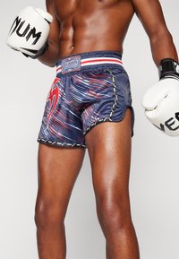 Marineblaue Venum-Boxershorts mit roten und weißen Linien, elastischem Bund und Seitenschlitzen für Bewegungsfreiheit. Mit Logo-Akzenten und Besatz.