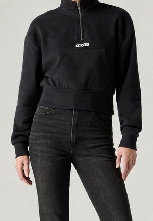 Black cropped Levi's quarter-zip sweatshirt with front pocket, worn with high-waisted black jeans on a standing person.