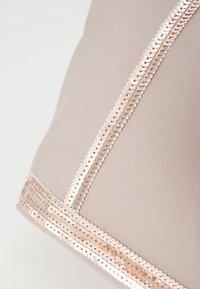 Ljust beige tyg med en strukturerad yta, med en remsa av roségulds-sekvenser längs sömmen för dekorativ detalj.