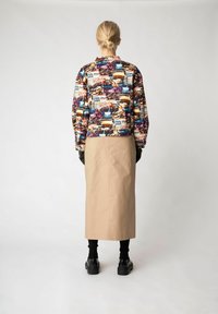 Multikleurige geprinte jas met stedelijke afbeeldingen, gecombineerd met een beige midi-rok, zwarte sokken en zwarte platform schoenen.