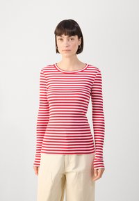 Red and white striped long-sleeve shirt with a round neckline and ribbed texture, paired with light-colored, relaxed-fit pants.